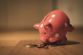 Alcancía de cerámica con forma de chancho rosado sobre una mesa de madera, simulando comer monedas.